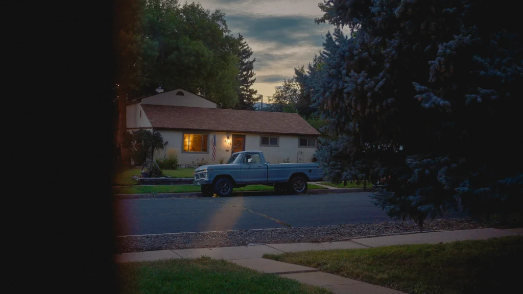 An old truck parked outside a 1950's home in the evening 